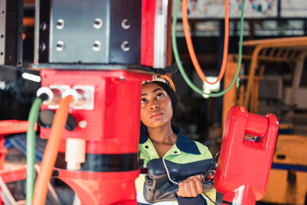Técnico industrial con casco y uniforme de seguridad realizando mantenimiento en instalaciones mecánicas pesadas.